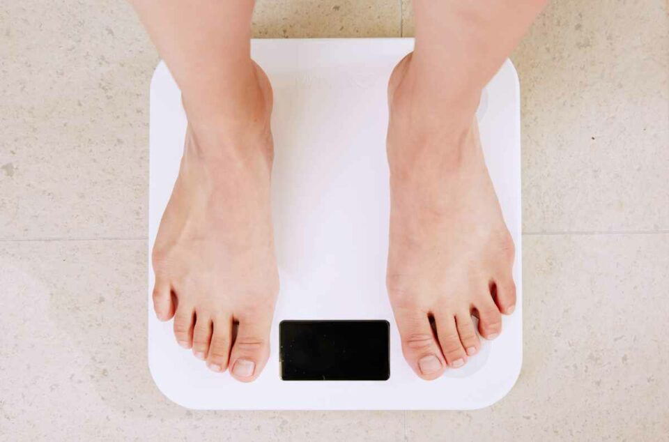 A person's bare feet standing on a white bathroom scale to measure BMI